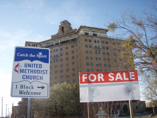 A For Sale sign and a United Methodist church sign give hope to the Baker Hotel.