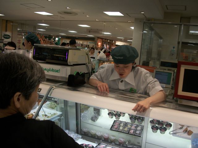 A food service worker helps a customer make a selection at a Japanese department store. Many department stores in Japan include complete grocery stores plus independent specialized shops.
