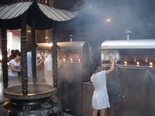 A young girl lights incense in the temple made for Matsu. It is located in the Dajia District of Taichung. Other young worshippers are to her left.