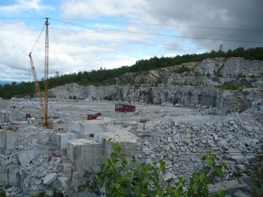 A derrick on the top of E. L. Smith Quarry at Graniteville, South Barre, Vermont, lifts blocks of granite and transports stone workers in and out of the quarry. Blocks weigh 40 tons each. The stone workers cut the blocks from granite benches 50 feet square and 10 feet deep. Granite weighs 170 lbs for each cubic foot.