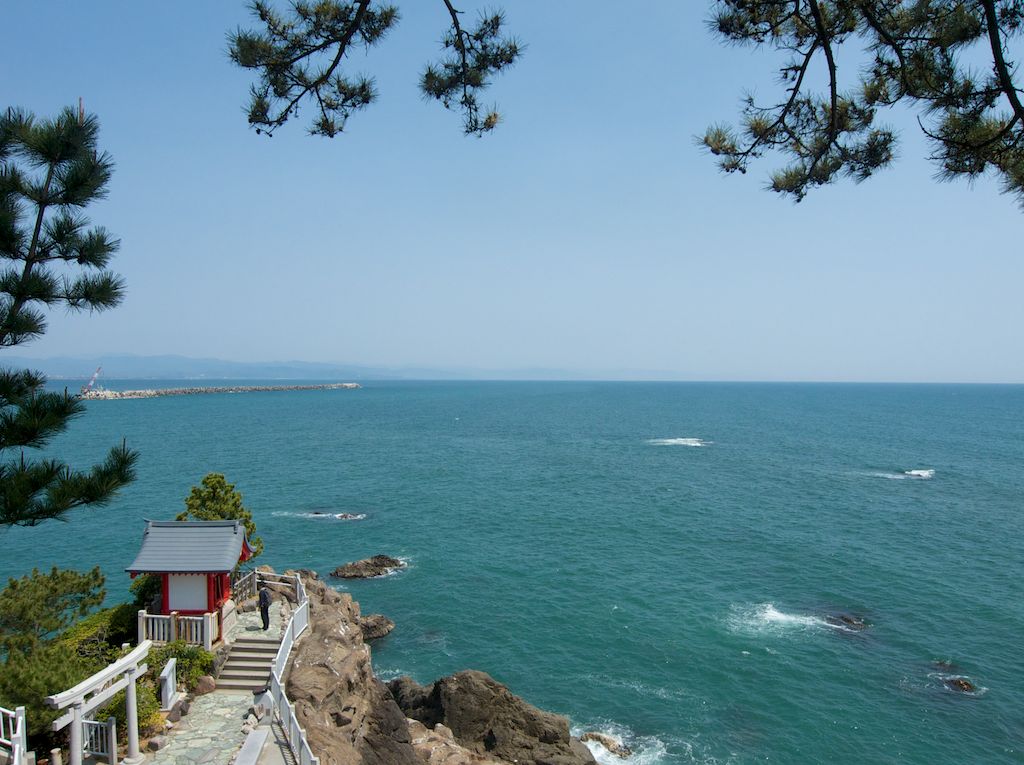 Looking East Across the Pacific. A tiny Shinto shrine perches atop a cliff overlooking the Pacific Ocean at Katsurahama Beach at Kochi. Hundreds of steps below, a paved sidewalk skirts the pea-sized gravel beachfront for a water level viewpoint of the surrounding ocean. 