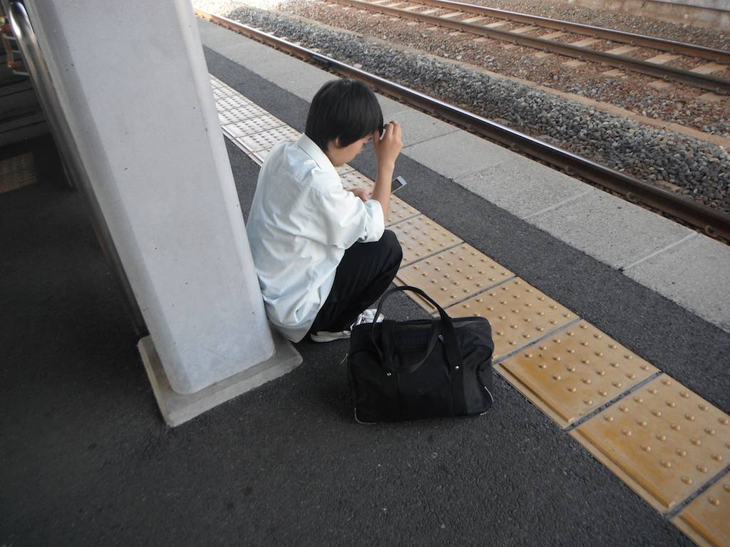 A Japanese Boy Uses Smartphone and Waits for Train